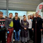 Grupa ludzi, w tym uczniowie w swetrach, zakonnica i duchowny, pozują w pomieszczeniu podczas wydarzenia.