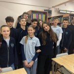 Grupa uczniów i nauczyciel pozują razem w bibliotece, uśmiechając się do kamery.