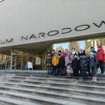 Grupa dzieci w zimowych ubraniach stoi na schodach przed budynkiem Muzeum Narodowego.