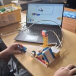 Dziecko buduje robota LEGO podłączonego do laptopa z instrukcjami kodowania na ekranie.