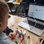 Dziecko buduje konstrukcję LEGO podłączoną do laptopa z uruchomionym programem do kodowania w klasie.