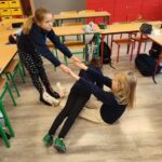 Trzy młode dziewczyny trzymają się za ręce i pochylają w klasie z biurkami i kolorowymi szafkami.