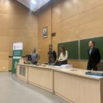 Cztery osoby stoją na podium sali wykładowej z zielonymi tablicami i banerem Wydziału Biologii.