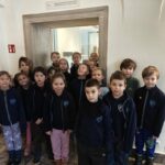 Grupa małych dzieci w szkolnych mundurkach stoi razem w pomieszczeniu, pozując do zdjęcia.