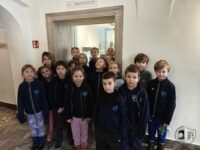 Grupa małych dzieci w szkolnych mundurkach stoi razem w pomieszczeniu, pozując do zdjęcia.