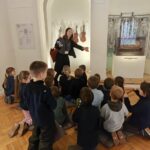 Kobieta objaśnia instrumenty muzyczne grupie dzieci siedzących na podłodze muzeum.