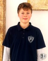 Chłopak z krótkimi kręconymi włosami ubrany w granatową koszulkę z białym emblematem poznańskiej szkoły SP7.