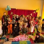 Grupa dzieci w kolorowych kostiumach pozuje razem w udekorowanej klasie.