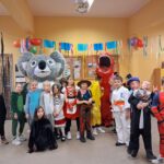 Grupa dzieci w kolorowych kostiumach pozujących w pomieszczeniu na przyjęciu z świątecznymi dekoracjami.