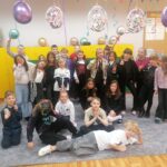Grupa dzieci pozuje radośnie w udekorowanej klasie z balonami i świątecznym wystrojem.