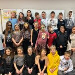 Grupa dzieci w kolorowych kostiumach i okularach przeciwsłonecznych pozuje razem w klasie.