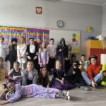 Dzieci w kolorowych kostiumach pozują razem w klasie ze świątecznymi dekoracjami i tablicą.