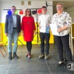 Cztery osoby stoją na scenie, dwie trzymają certyfikaty, a w tle widać kolorowe światła.