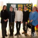 Pięć osób stoi w pomieszczeniu przed zieloną tablicą z żółtymi kształtami i papierami.