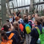 Grupa dzieci z plecakami słucha przewodniczki w szklarni z kaktusami.