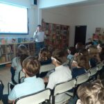 Grupa uczniów w okularach 3D ogląda prezentację mężczyzny w bibliotece.