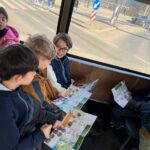 Czworo dzieci siedzących w autobusie, uśmiechniętych i patrzących na kolorowe mapy podczas wspólnej jazdy.