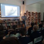 Mężczyzna prowadzi prezentację na temat statku dla grupy dzieci w bibliotece.