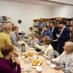 Grupa seniorów i studentów dzieli się jedzeniem i napojami przy stole w bibliotece.