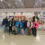 Grupa dzieci i dorosły pozują i uśmiechają się do siebie wewnątrz dużego budynku.