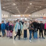 Grupa dzieci stoi w pomieszczeniu, pozując i uśmiechając się w dużej, jasnej hali wystawowej.