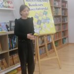 Dziecko recytuje podczas szkolnego konkursu w bibliotece, stojąc w pobliżu jaskrawożółtego plakatu wydarzenia.