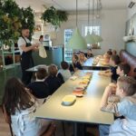 Szef kuchni demonstruje robienie pizzy grupie dzieci siedzących przy stole ze składnikami.