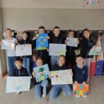 Dziesięcioro dzieci w szkolnych mundurkach dumnie prezentuje kolorowe rysunki, stojąc i klęcząc w pomieszczeniach.