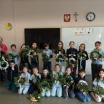 Grupa dzieci i nauczyciel trzymają udekorowane wieńce, pozując w klasie.