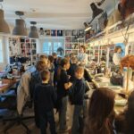 Grupa dzieci zwiedza warsztat pełen peruk, narzędzi i luster.