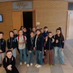 Grupa uczniów stoi razem przed wejściem do audytorium wewnątrz budynku.