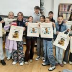 Grupa dzieci w bibliotece trzyma ilustrowane torby z kreskówkowymi zwierzętami i tekstem.