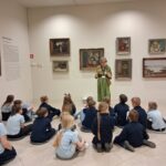 Kobieta przemawia do grupy dzieci siedzących na podłodze w galerii muzeum sztuki.