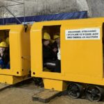 Dzieci w żółtych wózkach w kaskach, jadące małą podziemną kolejką górniczą.