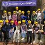 Grupa dzieci w żółtych kaskach pozuje przed transparentem Kopalni Soli Kłodawa.