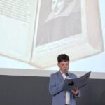 Chłopiec w niebieskiej marynarce czyta na głos, a za nim wyświetlana jest książka Szekspira.