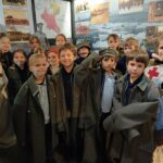 Grupa dzieci ubranych w historyczne stroje wojskowe pozuje razem na wystawie muzealnej.