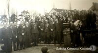 Grupa umundurowanych mężczyzn pozuje przed budynkiem; napis Szkoła Korpusu Kadetów.