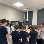 Grupa uczniów ogląda pokaz medyczny z użyciem manekina w sali symulacji klinicznych.