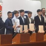 Siedmiu młodych mężczyzn i dwóch dorosłych stoi w rzędzie trzymając certyfikaty podczas ceremonii wręczenia nagród.