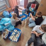 Czworo dzieci siedzi na podłodze, sortując i układając papierowe kubki, otoczone torbami i przyborami.