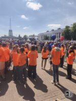 Tłum na imprezie plenerowej; ludzie w pomarańczowych koszulkach CREW stoją na pierwszym planie twarzą do sceny.