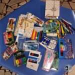 Różne przybory szkolne, materiały plastyczne i artykuły papiernicze rozłożone na niebieskim stole.