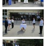 Uczniowie i nauczyciele stoją przed budynkiem szkoły podczas ceremonii, zgromadzeni przy stole.