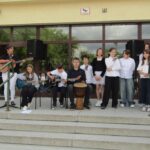 Grupa studentów gra na gitarach i bębnach na zewnątrz budynku na klatce schodowej.