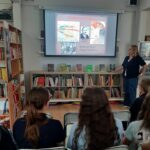 Kobieta prezentuje pokaz slajdów poświęcony stalinizmowi w Polsce grupie osób siedzących w bibliotece.