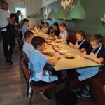 Dzieci w fartuszkach siedzą przy stoliku w restauracji i przygotowują pizzę.