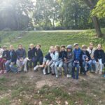 Grupa dzieci siedzących w rzędzie na ławce w parku.