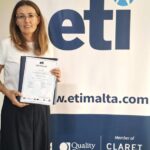 Kobieta trzymająca certyfikat ETI przed banerem firmy.